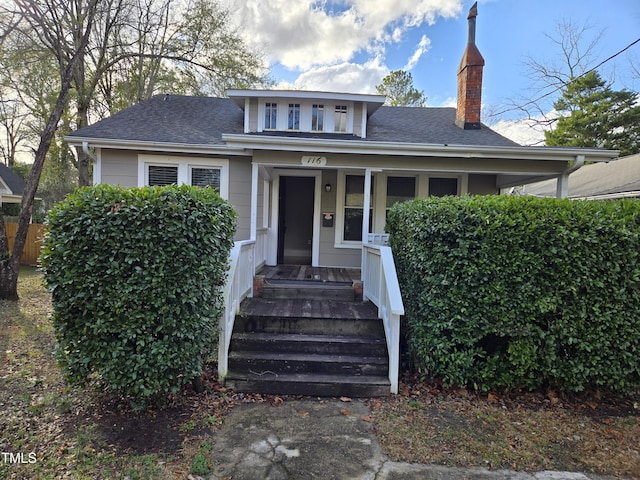 bungalow-style house with covered porch, a chimney, and roof with shingles