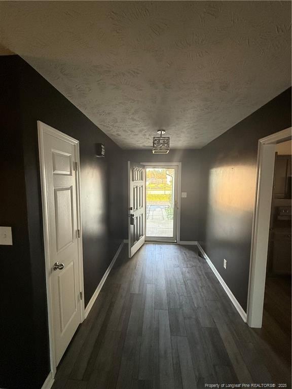 doorway featuring dark wood-type flooring, a textured ceiling, and baseboards