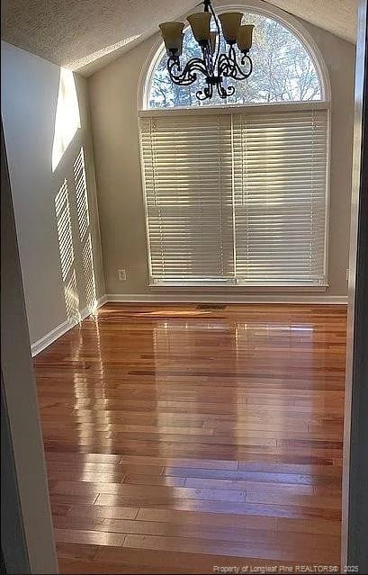 unfurnished dining area with a textured ceiling, lofted ceiling, a notable chandelier, wood finished floors, and baseboards