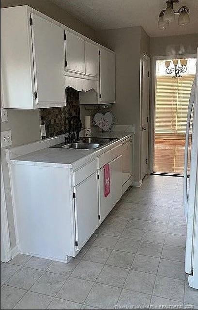 kitchen with white appliances, white cabinetry, light countertops, and a sink