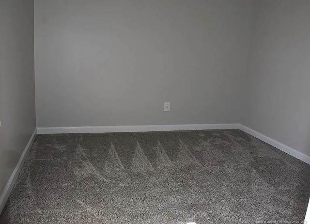 empty room featuring dark colored carpet and baseboards