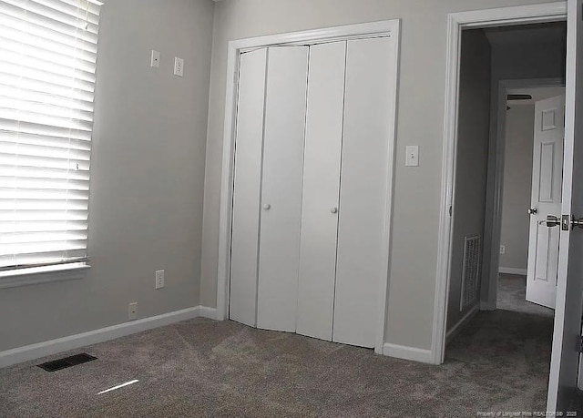 unfurnished bedroom with a closet, visible vents, dark carpet, and multiple windows