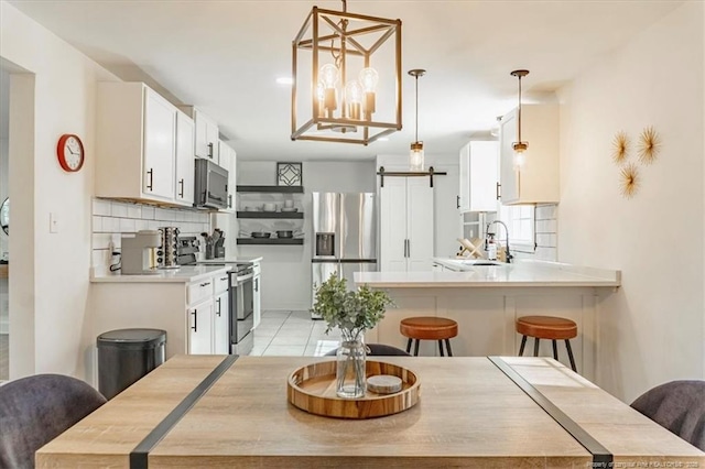 kitchen with a breakfast bar area, stainless steel appliances, light countertops, white cabinetry, and backsplash