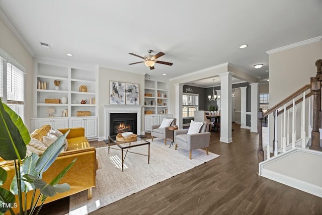 living room with dark wood-style flooring, stairway, ornate columns, a glass covered fireplace, and crown molding