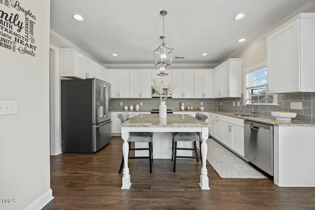 kitchen with stainless steel appliances, a sink, a kitchen island, white cabinets, and decorative light fixtures