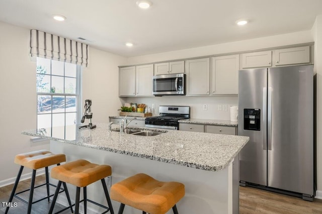 kitchen featuring gray cabinets, light stone counters, stainless steel appliances, and a sink