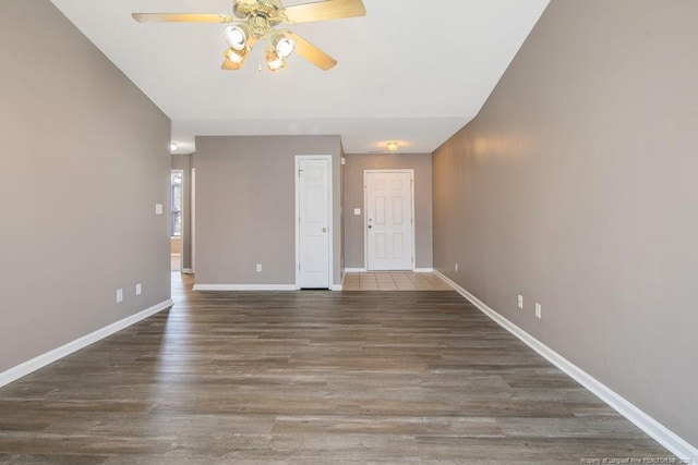 empty room featuring a ceiling fan, baseboards, and dark wood-style flooring