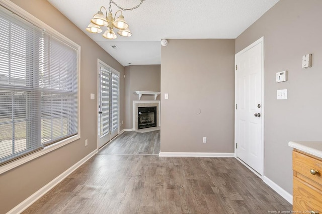 unfurnished living room with a chandelier, dark wood-style flooring, a fireplace, visible vents, and baseboards