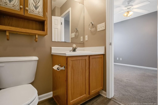 half bathroom featuring toilet, baseboards, a ceiling fan, and vanity