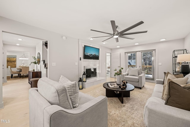 living area featuring a large fireplace, light wood finished floors, a ceiling fan, and recessed lighting