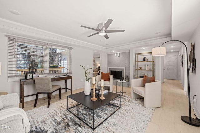 living room with a large fireplace, baseboards, ceiling fan, ornamental molding, and light wood-type flooring