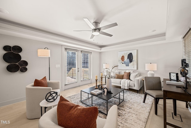 living area featuring light wood finished floors, baseboards, ceiling fan, a tray ceiling, and french doors