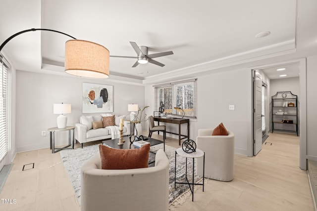 living room featuring light wood-style floors, a raised ceiling, a ceiling fan, and baseboards