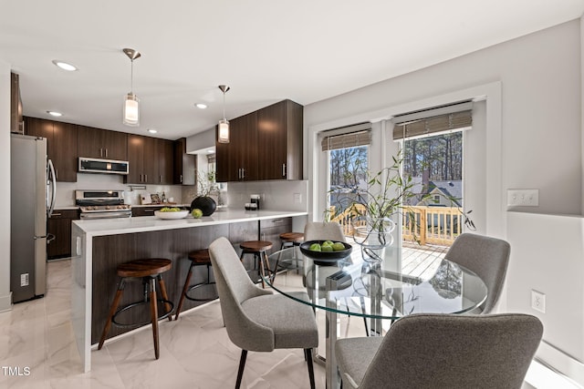 kitchen featuring stainless steel appliances, a peninsula, dark brown cabinets, light countertops, and a kitchen bar