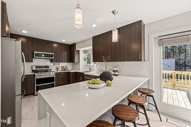 kitchen featuring marble finish floor, stainless steel appliances, a sink, dark brown cabinets, and a peninsula