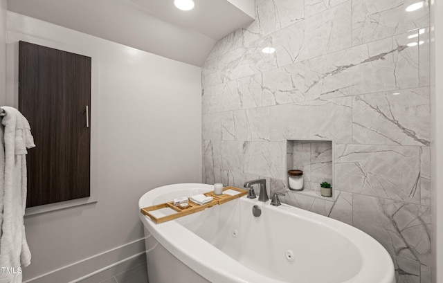 full bathroom with lofted ceiling, a soaking tub, and baseboards