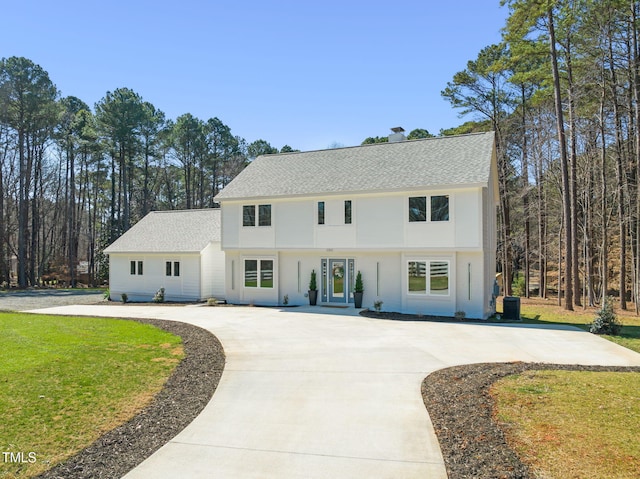 colonial inspired home featuring central air condition unit, curved driveway, a front lawn, and roof with shingles