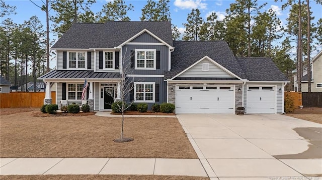 craftsman-style home featuring an attached garage, covered porch, fence, concrete driveway, and a standing seam roof