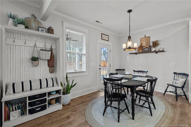 dining room featuring a chandelier, wood finished floors, visible vents, baseboards, and ornamental molding