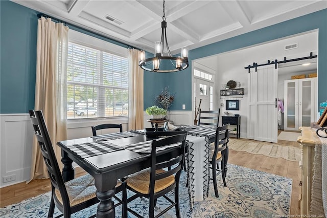 dining room featuring a barn door, visible vents, coffered ceiling, and wood finished floors