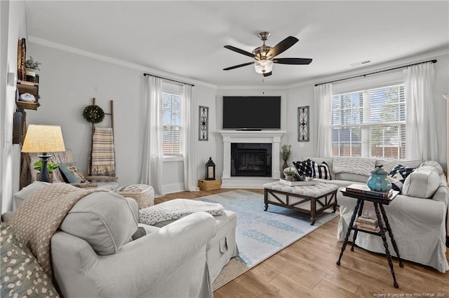 living room featuring light wood-type flooring, ornamental molding, a wealth of natural light, and a glass covered fireplace