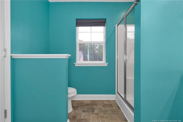 full bathroom featuring toilet, a shower stall, baseboards, and stone finish flooring