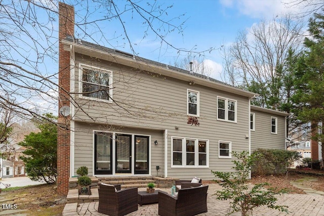 back of house with an outdoor living space, a patio, and a chimney