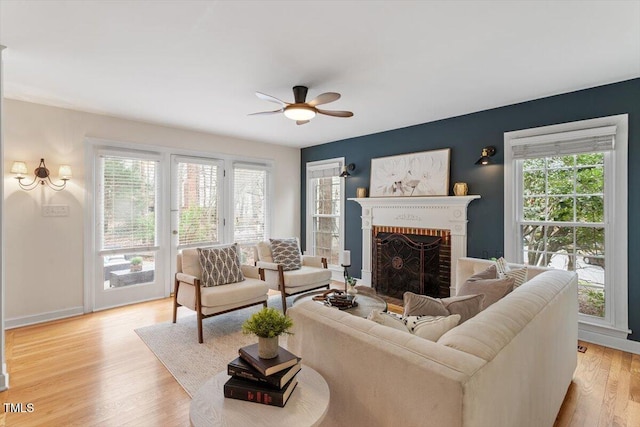 living area with a brick fireplace, light wood finished floors, a ceiling fan, and a wealth of natural light