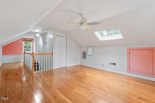 additional living space with light wood-type flooring, visible vents, lofted ceiling with skylight, and ceiling fan