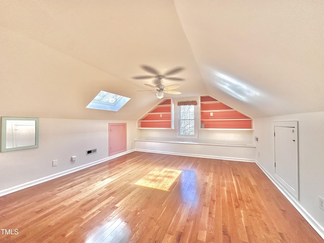 additional living space with visible vents, baseboards, vaulted ceiling with skylight, ceiling fan, and light wood-style floors