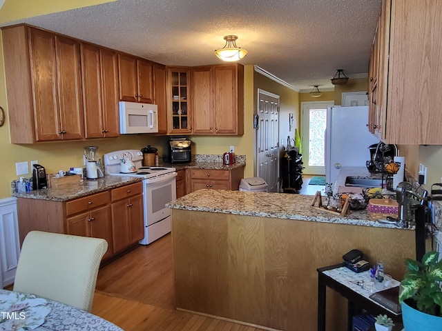 kitchen featuring a peninsula, white appliances, glass insert cabinets, and brown cabinetry