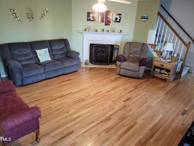 living area featuring a fireplace, stairway, and light wood finished floors