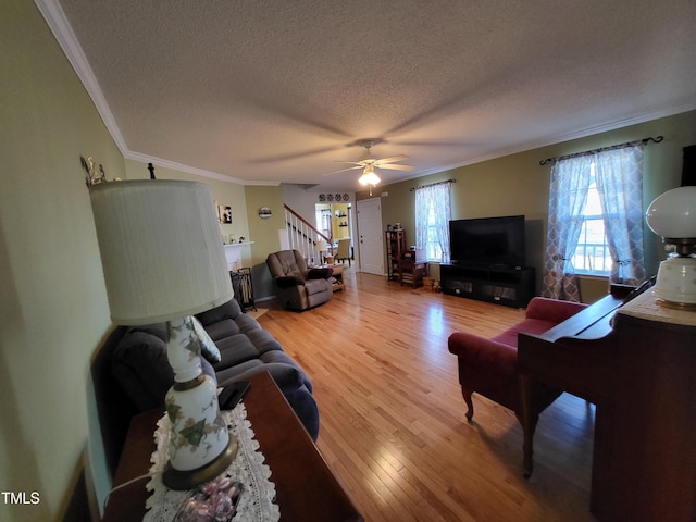 living area featuring a textured ceiling, wood finished floors, a ceiling fan, stairway, and crown molding