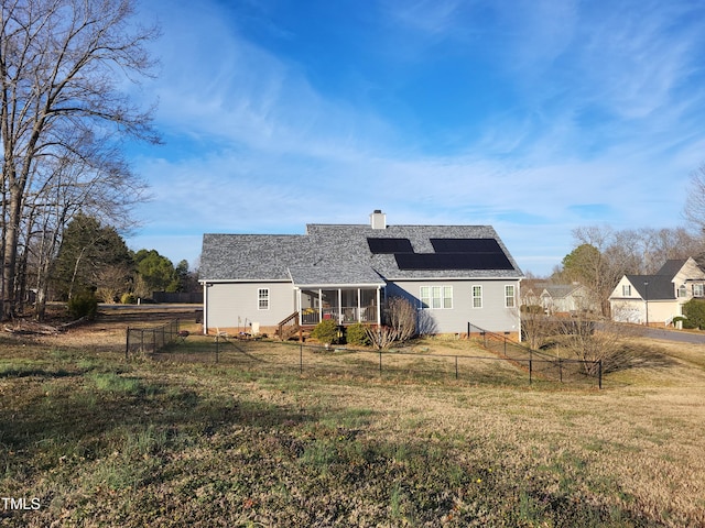 back of property with a yard, a chimney, a fenced backyard, and roof mounted solar panels