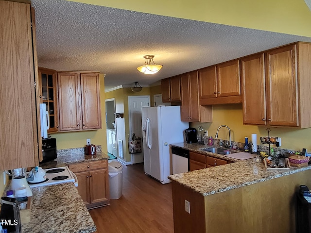 kitchen with light stone counters, a peninsula, white appliances, a sink, and brown cabinetry