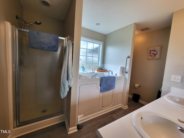 bathroom featuring a bath, a sink, a textured ceiling, a stall shower, and wood finished floors