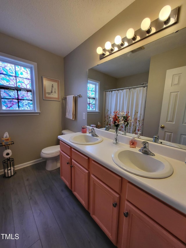 bathroom with toilet, wood finished floors, a sink, and double vanity