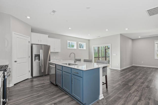 kitchen featuring a sink, white cabinets, light countertops, appliances with stainless steel finishes, and a center island with sink