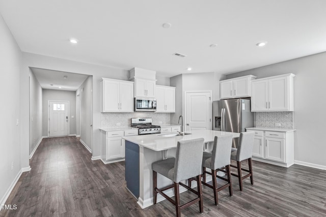 kitchen featuring light countertops, appliances with stainless steel finishes, white cabinetry, an island with sink, and a kitchen bar