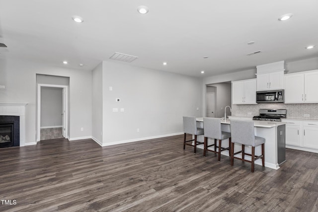 kitchen featuring light countertops, appliances with stainless steel finishes, a kitchen island with sink, white cabinetry, and a kitchen breakfast bar