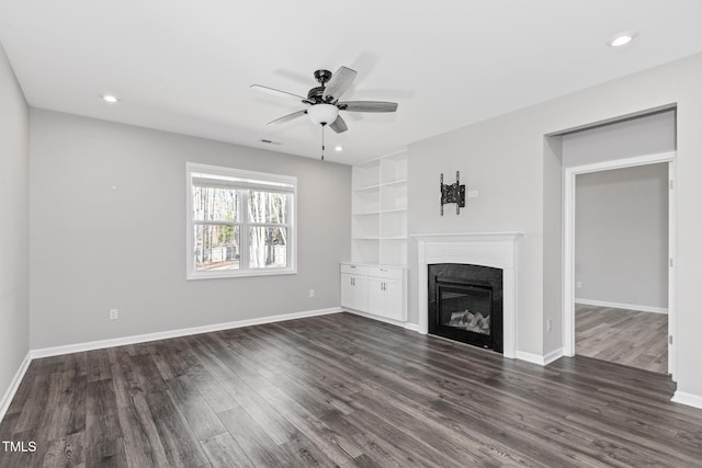 unfurnished living room with recessed lighting, a glass covered fireplace, dark wood finished floors, and baseboards