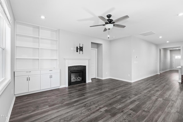 unfurnished living room featuring dark wood-style floors, a glass covered fireplace, and baseboards