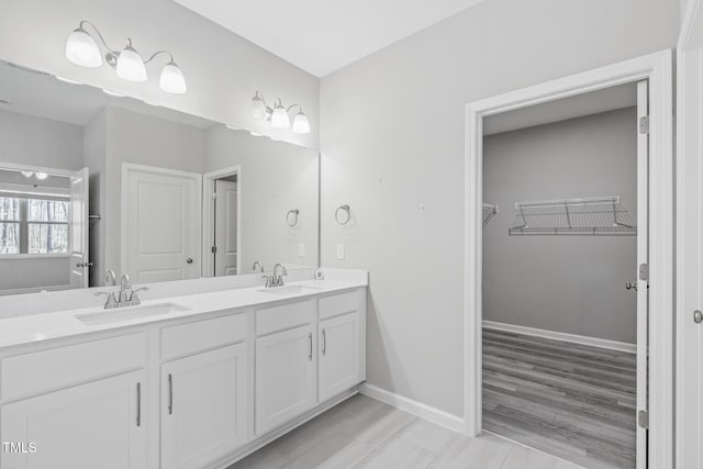 bathroom with a spacious closet, double vanity, a sink, and baseboards