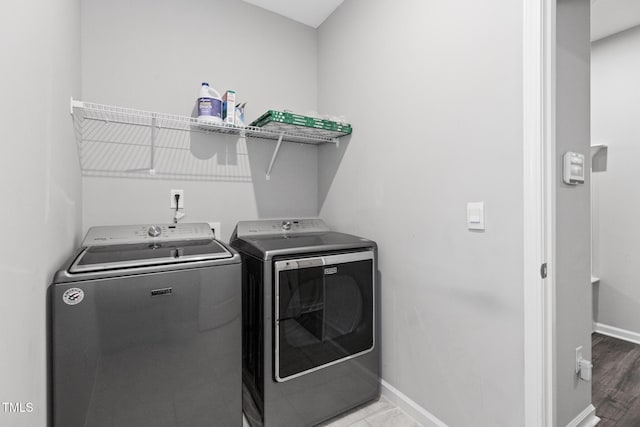 washroom featuring washing machine and dryer, laundry area, baseboards, and wood finished floors