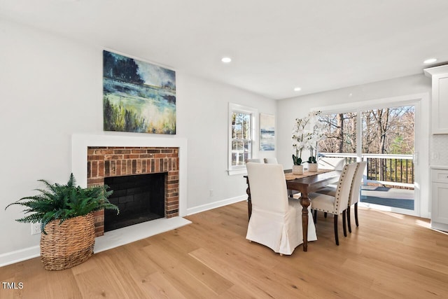 dining space with a wealth of natural light, a brick fireplace, baseboards, and light wood finished floors