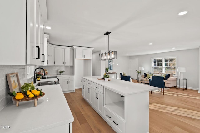 kitchen with a sink, a kitchen island, white cabinets, and light countertops