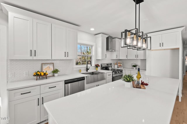 kitchen with light countertops, hanging light fixtures, appliances with stainless steel finishes, white cabinetry, and wall chimney exhaust hood