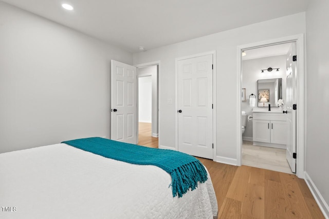 bedroom with light wood-style floors, ensuite bath, baseboards, and recessed lighting