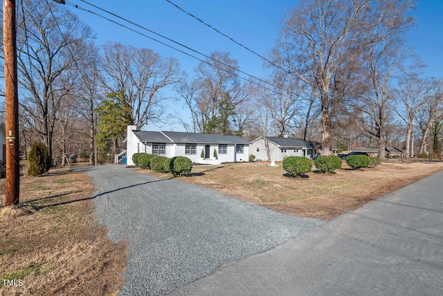 ranch-style home featuring driveway, a chimney, and a front yard