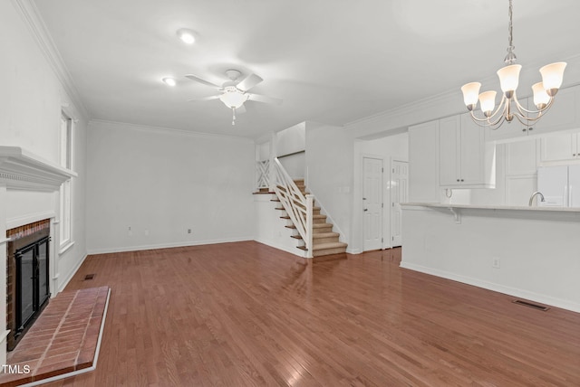 unfurnished living room featuring a fireplace, visible vents, ornamental molding, wood finished floors, and stairs